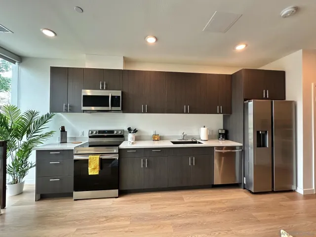 a large kitchen with stainless steel appliances granite countertop a stove top oven a sink dishwasher a refrigerator and a microwave oven on the wooden floor