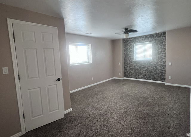 2815 Gordon Creek Road Price, UT 84501 - Photo 7 of 13 Spacious room featuring textured accent wall, two windows with blinds, ceiling fan, and dark carpet flooring