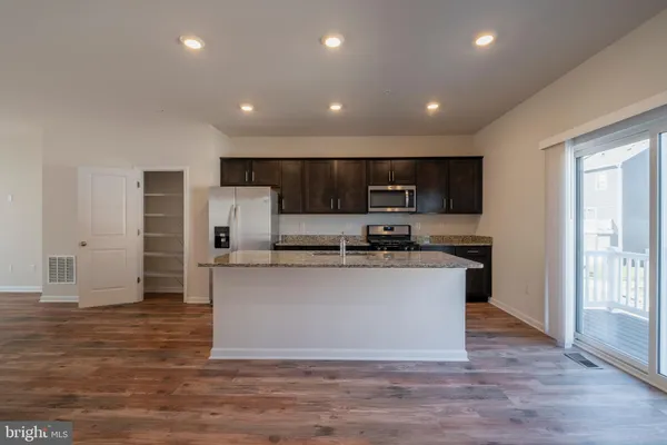 a kitchen with stainless steel appliances granite countertop a stove a sink a refrigerator white cabinets and wooden floor
