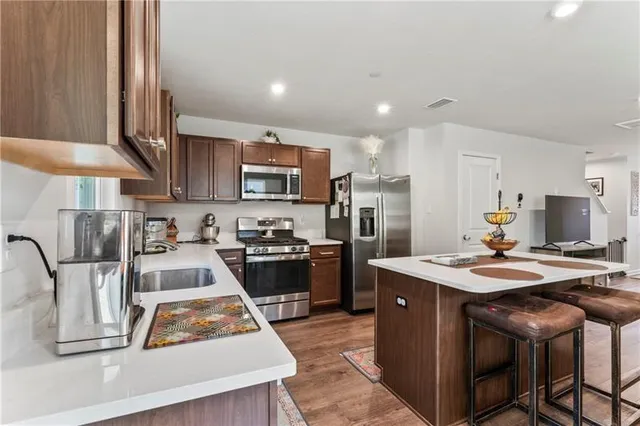 a kitchen with stainless steel appliances granite countertop a stove top oven a sink dishwasher a dining table and chairs with wooden floor