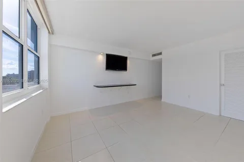 a view of an empty room with tv and kitchen view