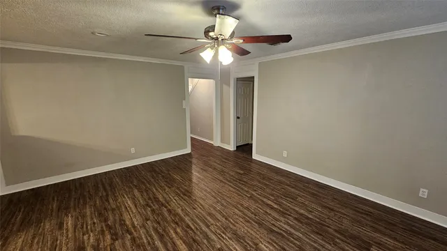 a view of an empty room with wooden floor and a ceiling fan