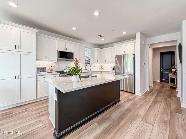 a kitchen with stainless steel appliances granite countertop a stove a refrigerator a microwave a dining table and chairs with wooden floor