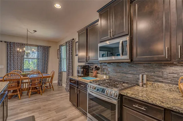 a kitchen with stainless steel appliances granite countertop a stove top oven a sink dishwasher a dining table and chairs with wooden floor