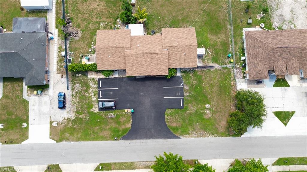 1940 48th Street Southwest Naples, FL 34116 - Photo 7 of 33 Property featuring a newly paved parking area with marked spaces, a multi-section shingle roof, and surrounding undeveloped green space