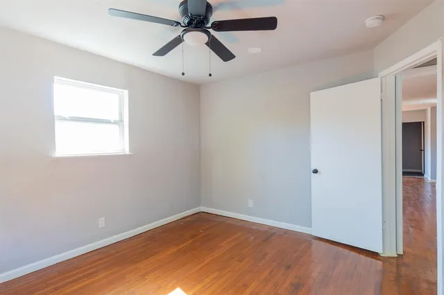 an empty room with wooden floor ceiling fan and windows