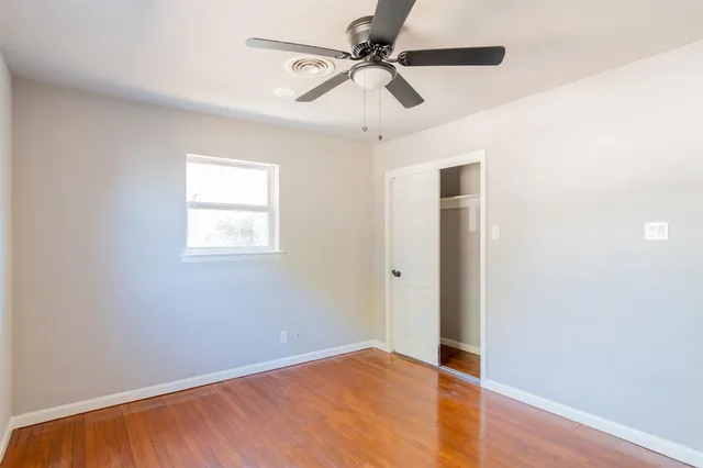 an empty room with wooden floor fan and windows