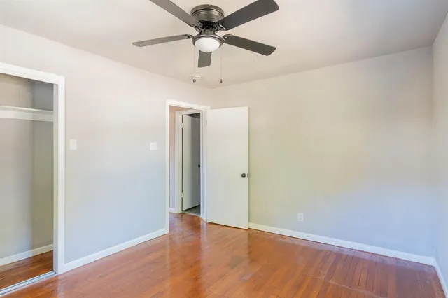 an empty room with wooden floor ceiling fan and windows
