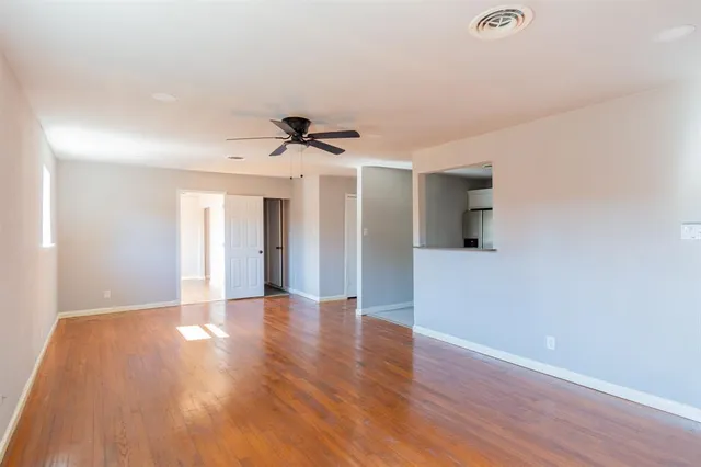 a view of an empty room with wooden floor and a ceiling fan