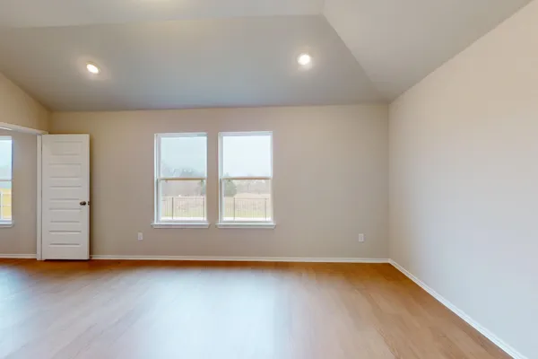 an empty room with wooden floor and windows with curtains