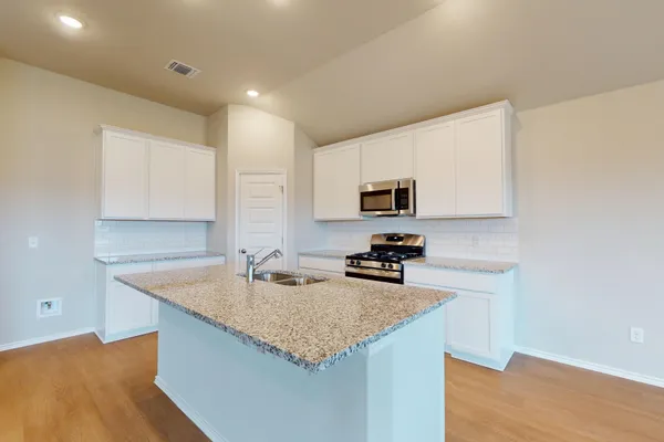 a kitchen with granite countertop a sink a stove counter space and cabinets