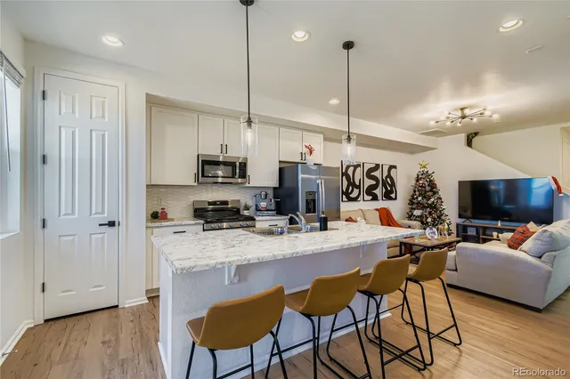 a kitchen with stainless steel appliances granite countertop a stove top oven a refrigerator a sink and chairs with wooden floor