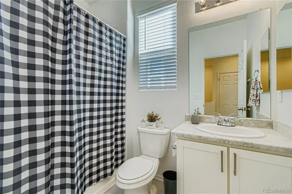 a bathroom with a granite countertop toilet a sink a mirror and shower curtain