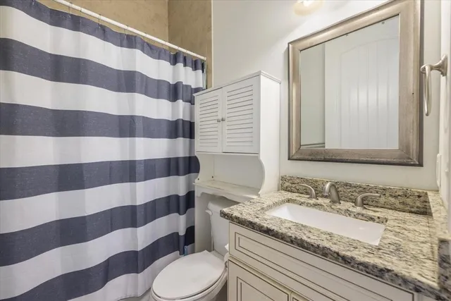 a bathroom with a granite countertop sink a toilet a mirror and shower curtain