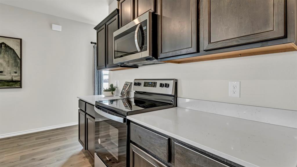 124 Pheasant Run Road Terrell, TX 75160 - Photo 23 of 35 Modern kitchen featuring dark wood-finish cabinetry, light stone countertops, stainless steel microwave, and a black electric range with a glass cooktop