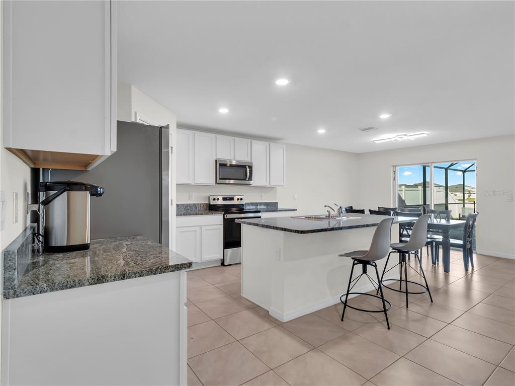 5446 Logan Cave Avenue Wimauma, FL 33598 - Photo 9 of 57 a kitchen with stainless steel appliances granite countertop a table chairs sink and cabinets