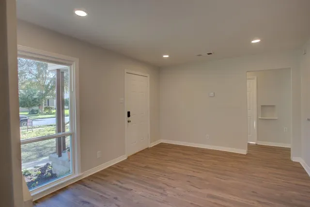 a view of an empty room with wooden floor and a window