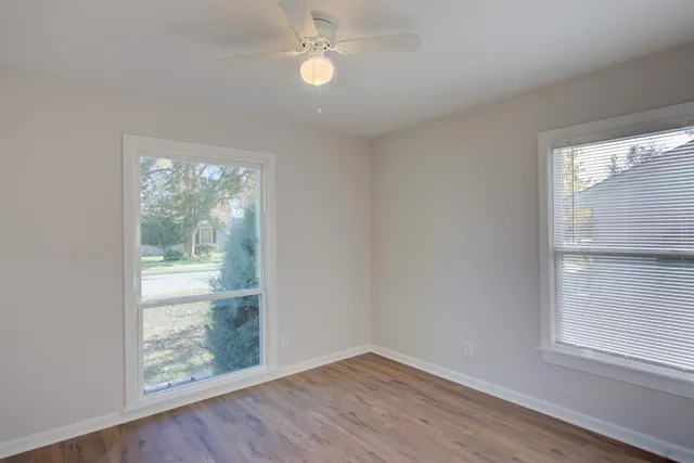 an empty room with wooden floor fan and windows