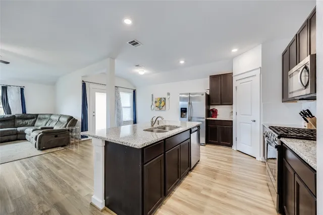 a kitchen with stainless steel appliances granite countertop a stove top oven a refrigerator a sink dishwasher and a dining table with wooden floor