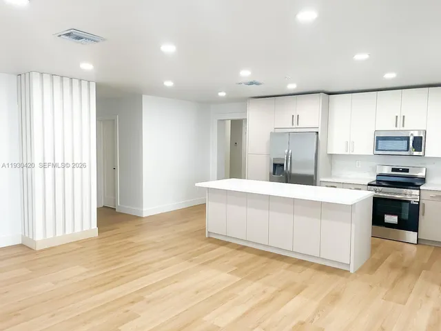 a large white kitchen with stainless steel appliances granite countertop a stove a sink and a refrigerator