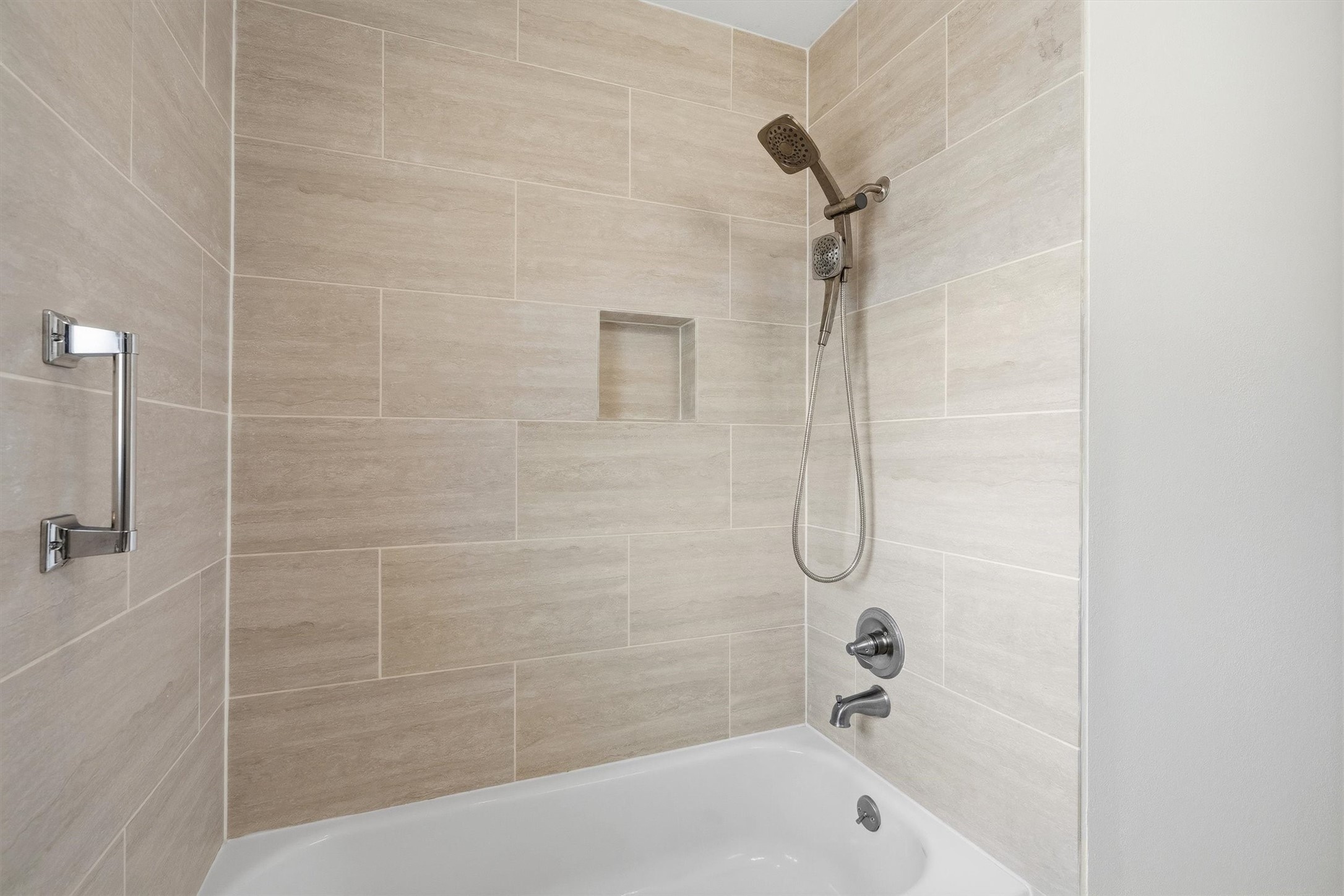 3331 Arbor Street Houston, TX 77004 - Photo 20 of 30 This showcases a modern shower-tub combo with sleek, neutral-toned tiles and a handheld showerhead. A built-in niche offers convenient storage, and a sturdy grab bar adds safety.