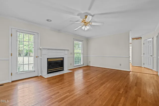 an empty room with wooden floor fireplace and windows