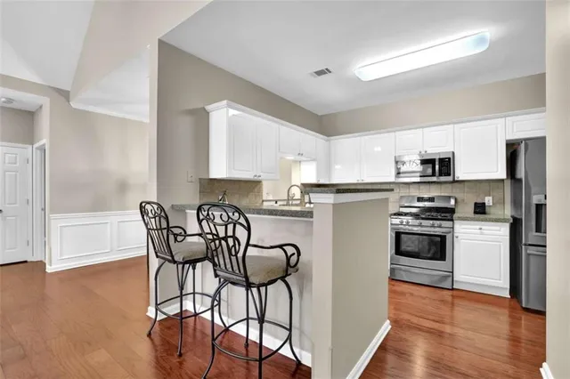 a kitchen with stainless steel appliances granite countertop a stove top oven a refrigerator a dining table and chairs with wooden floor