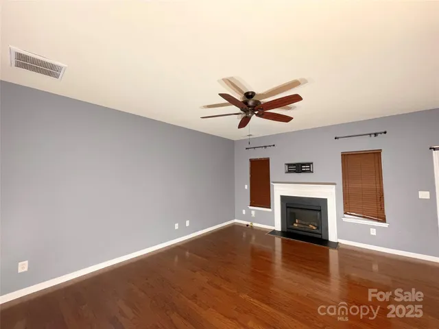 a view of a livingroom with a fireplace a ceiling fan and wooden floor