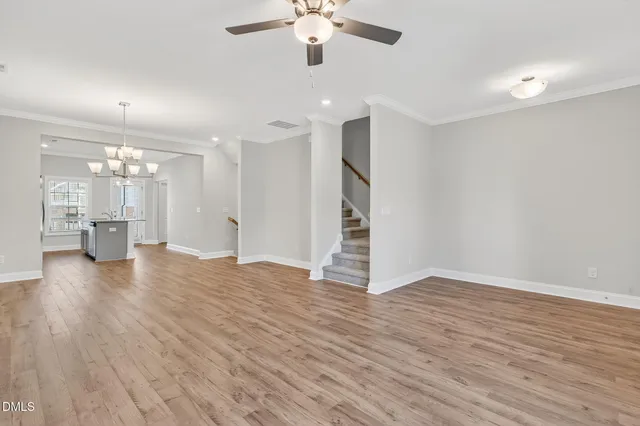 a view of an empty room with wooden floor and a kitchen
