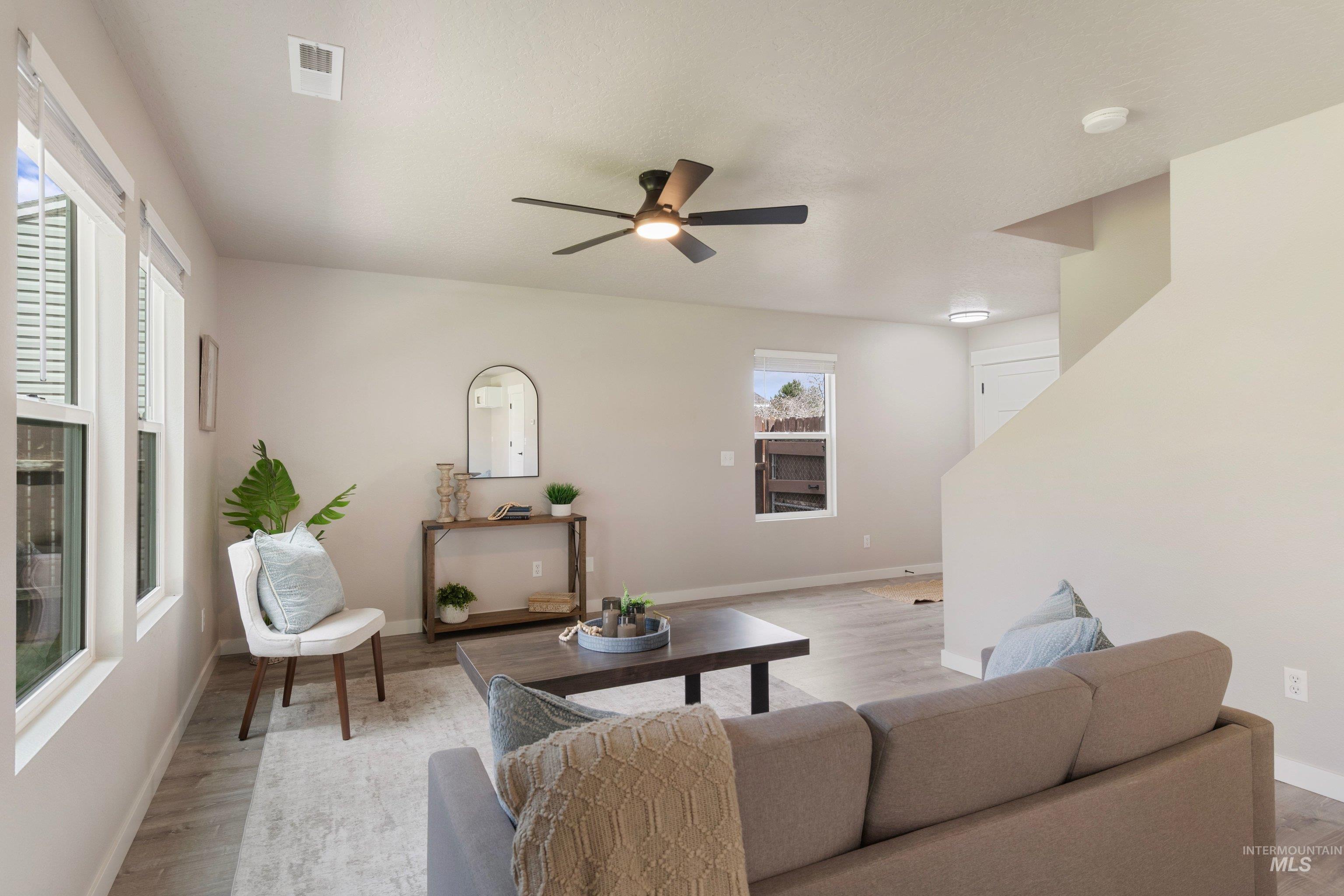 16759 Abram Avenue Caldwell, ID 83607 - Photo 8 of 33 Living area featuring wood-finish flooring, a contemporary ceiling fan with integrated lighting, multiple windows providing ample natural light, neutral wall colors, and a partial staircase