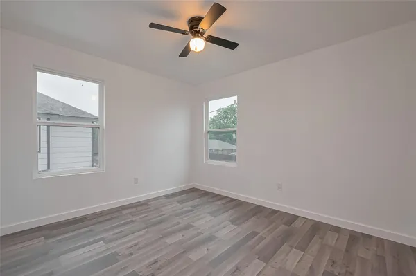 an empty room with wooden floor ceiling fan and windows