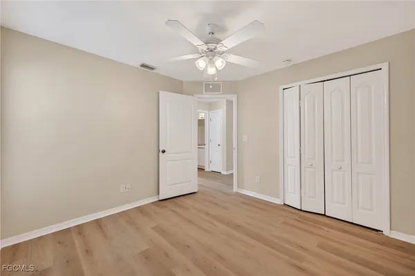 an empty room with wooden floor closet fan and windows