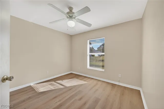 an empty room with wooden floor chandelier fan and windows