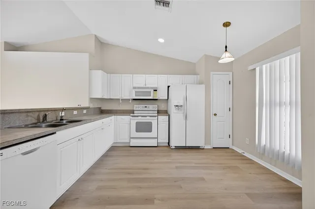 a large kitchen with granite countertop a white refrigerator oven a sink dishwasher and white cabinets with wooden floor