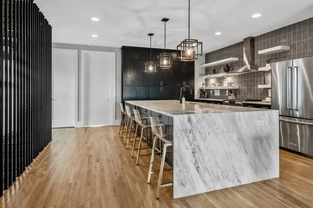 a kitchen with stainless steel appliances kitchen island granite countertop a refrigerator a stove and a wooden floors