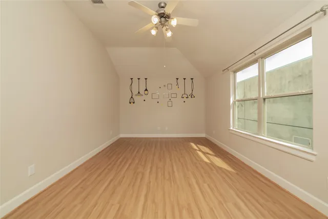 an empty room with wooden floor chandelier fan and windows