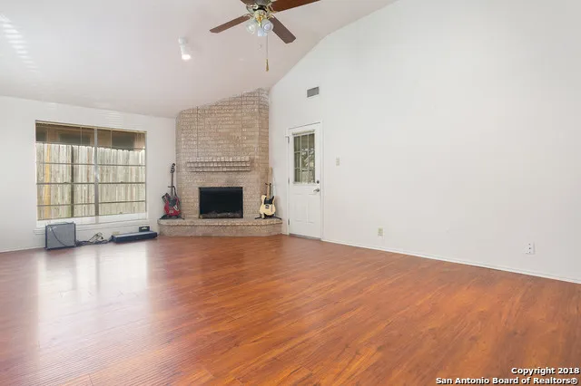 an empty room with wooden floor fireplace and windows