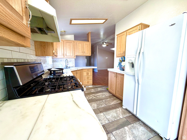 1025 North 300 West, Unit 1 Springville, UT 84663 - Photo 11 of 35 Kitchen with white fridge with ice dispenser, lofted ceiling, decorative backsplash, stainless steel range with gas stovetop, and under cabinet range hood