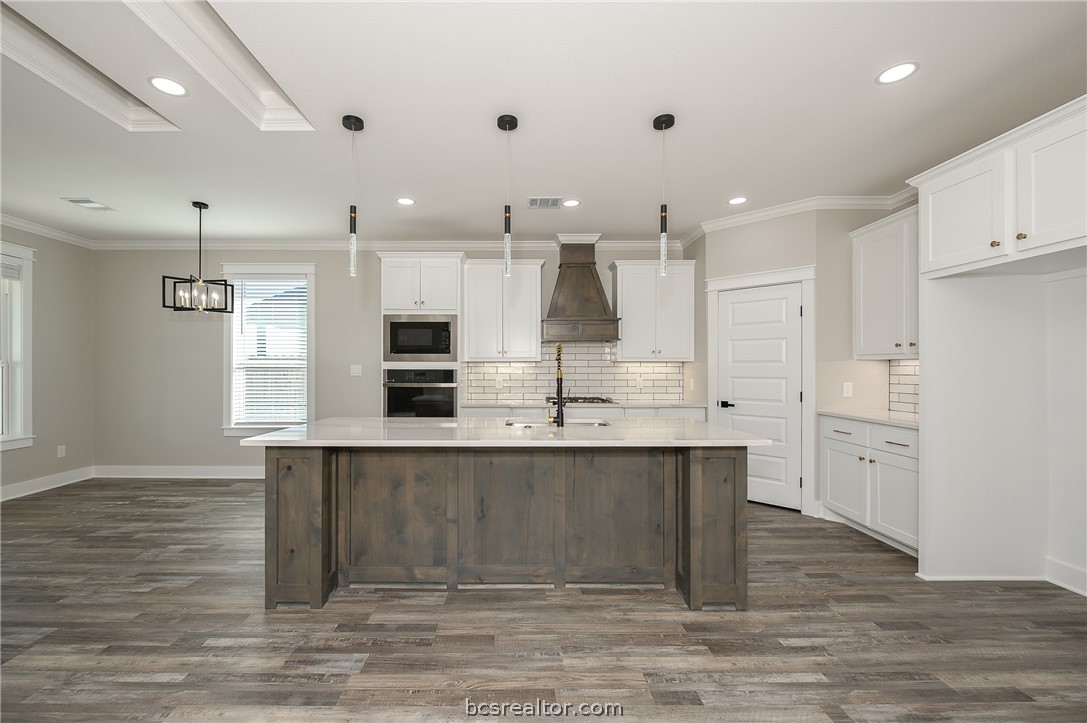 2908 GOLDBERG Drive Bryan, TX 77808 - Photo 24 of 44 Modern kitchen features: stainless steel appliances, quartz countertops, stained island, painted cabinets, decorative pendant lights, cabinet hardware, vinyl flooring, and tile backsplash.