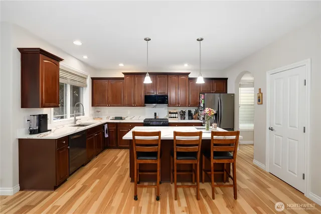 a kitchen with stainless steel appliances granite countertop a kitchen island a stove a refrigerator a sink a dining table and chairs with wooden floor