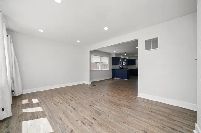 a view of empty room with wooden floor and kitchen