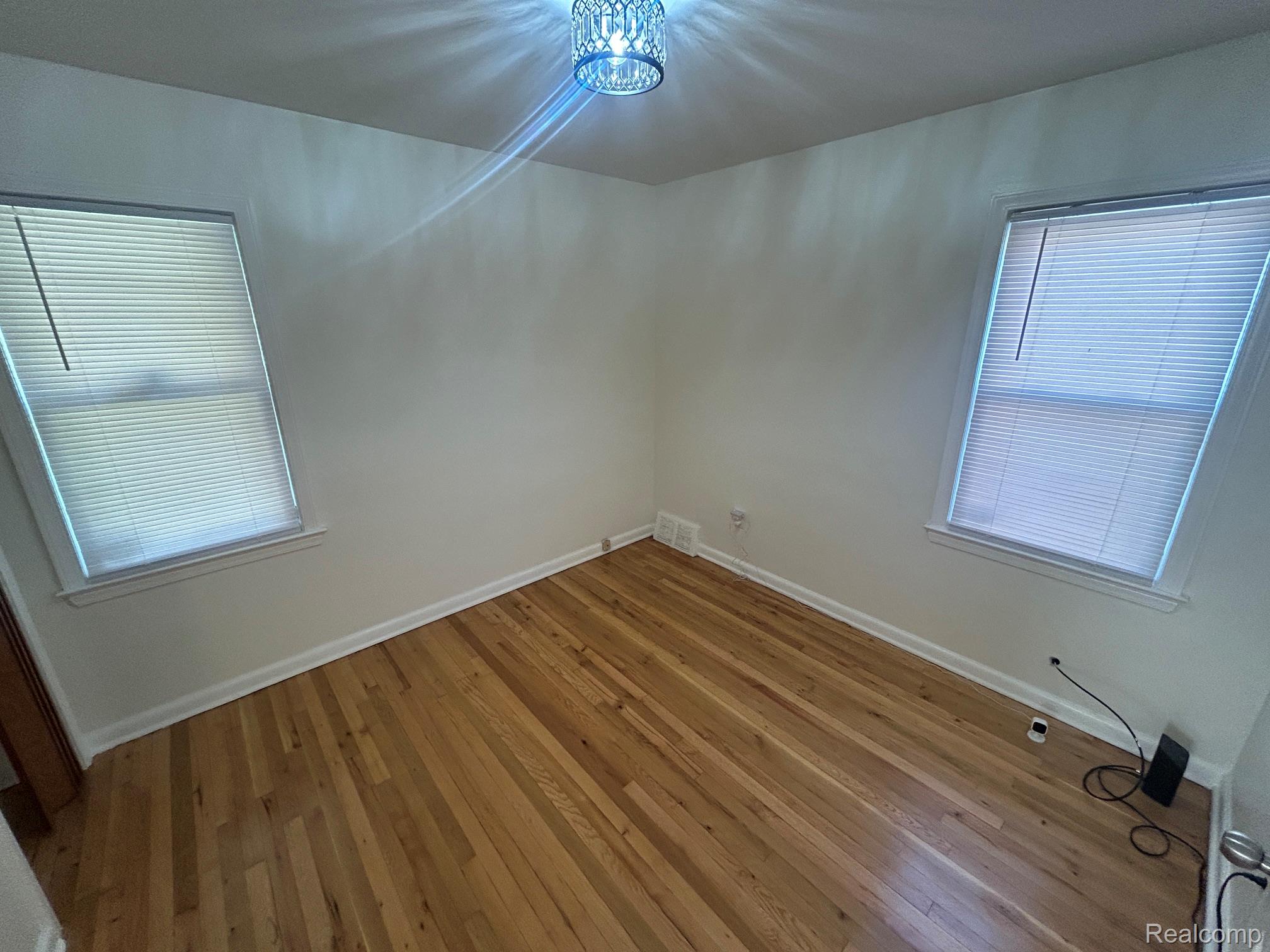 21970 Moross Road Grosse Pointe, MI 48236 - Photo 10 of 21 Hardwood flooring throughout, featuring two windows with horizontal blinds, a white ceiling, and a decorative ceiling light fixture