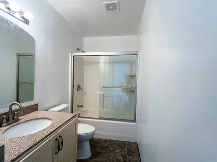 a bathroom with a granite countertop sink a toilet a mirror and shower