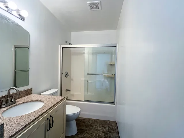 a bathroom with a granite countertop sink a toilet a mirror and shower