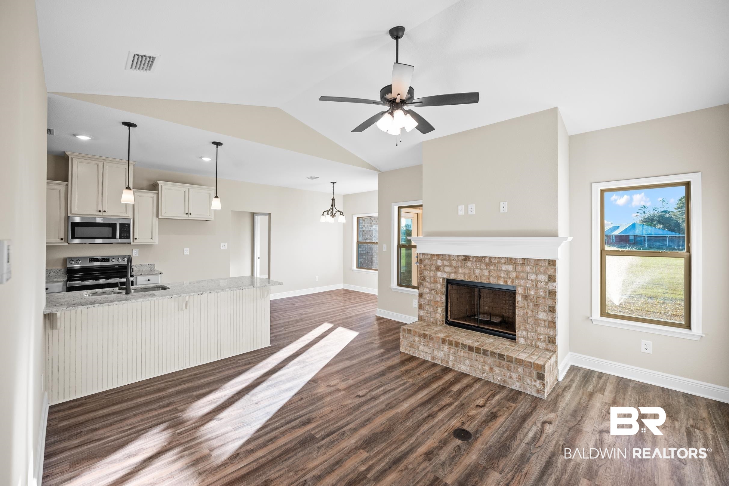 12833 Ward Road West Stapleton, AL 36578 - Photo 3 of 27 Unfurnished living room with dark wood-style floors, vaulted ceiling, a brick fireplace, a chandelier, and a ceiling fan