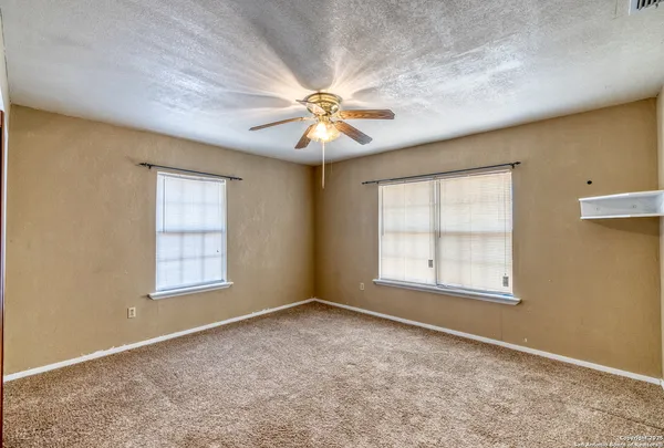 an empty room with chandelier fan and windows