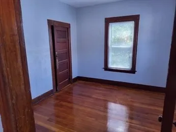 a view of an empty room with wooden floor and a window