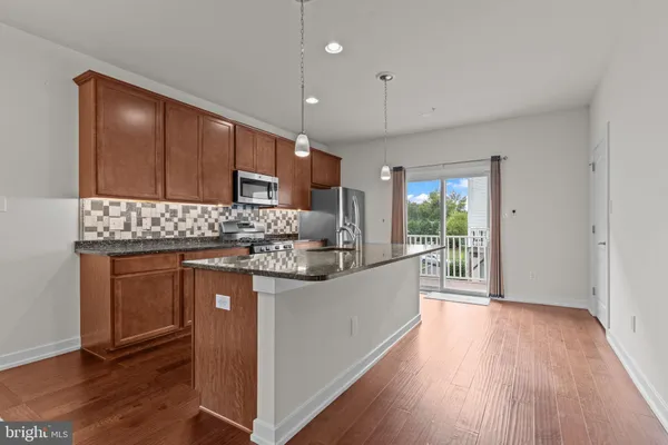 a kitchen with granite countertop wooden floors wooden cabinets and stainless steel appliances