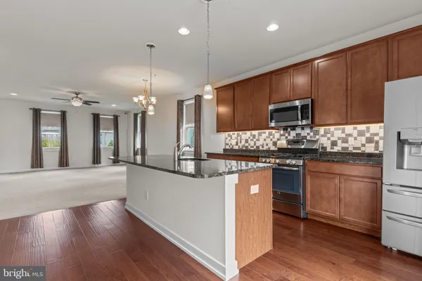 a kitchen with stainless steel appliances kitchen island granite countertop a stove a sink a refrigerator and a wooden floor