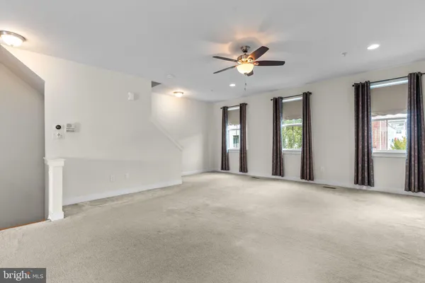 a view of an empty room with chandelier fan and windows